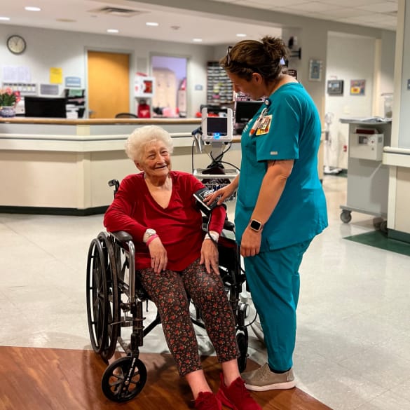 A senior resident smiling with a caregiver in a facility hallway