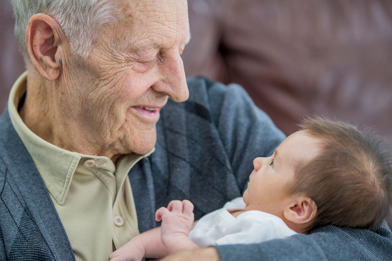 Elderly man holding a baby, smiling warmly.