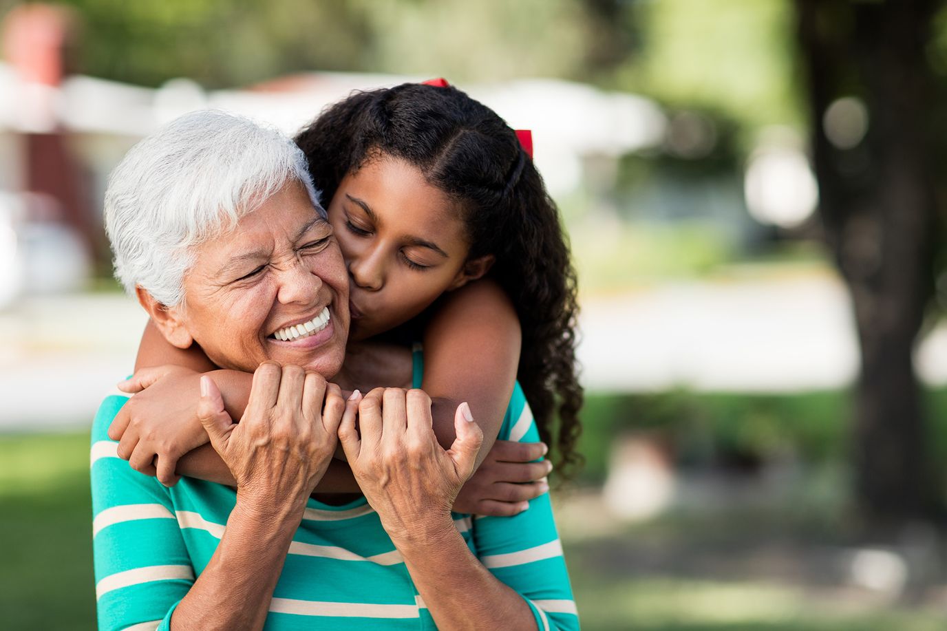 Smiling senior woman embraced by a young girl outdoors.