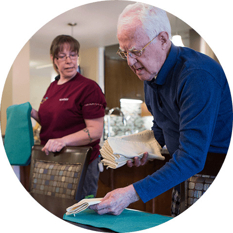 An elderly resident and staff member preparing dining area