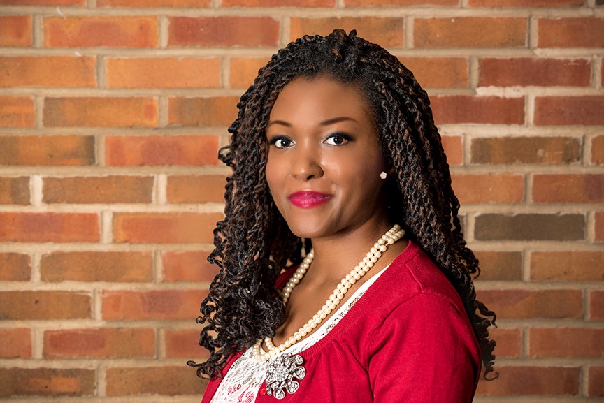 Portrait of a woman with braided hair in front of a brick wall