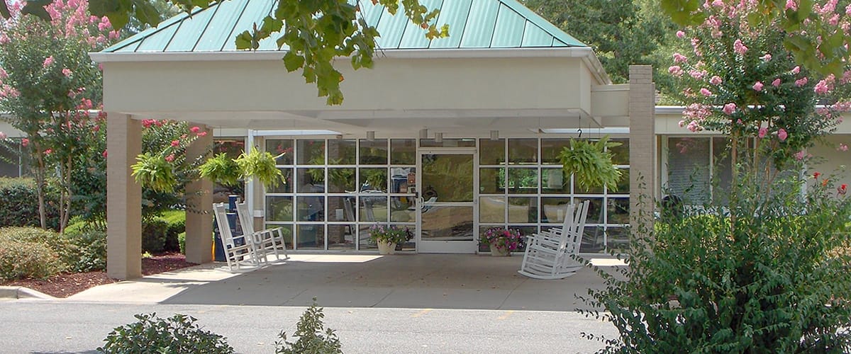 Entrance of a senior care facility with rocking chairs and greenery