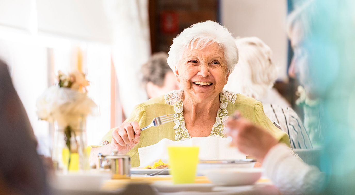 A smiling resident enjoying a meal at a dining table