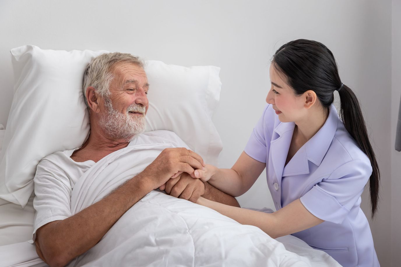 Nurse interacting warmly with elderly patient in bed.
