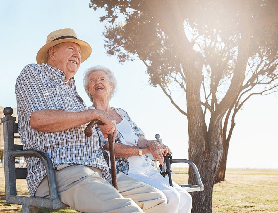 Two smiling seniors sitting on a bench under a tree