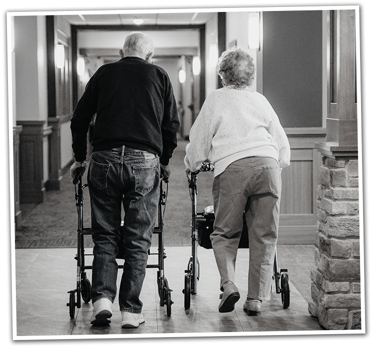 Two residents walking with walkers in a hallway