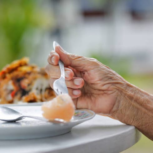 Close-up of a senior's hand holding a spoon with food