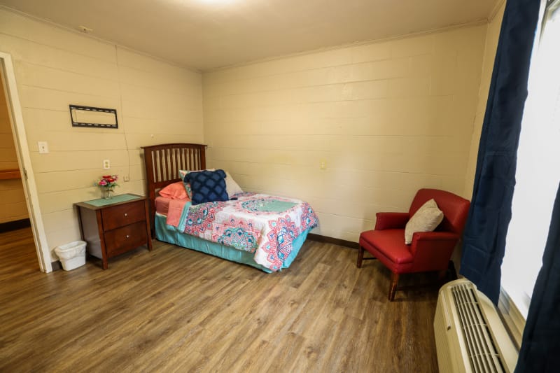 A cozy private resident room with a bed and chair