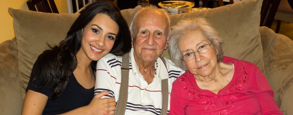 A caregiver poses with two senior residents on a couch