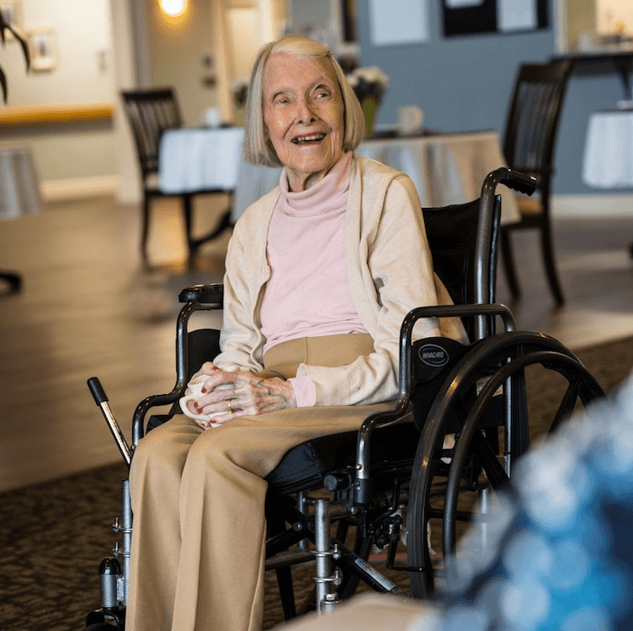 An elderly woman smiling in a wheelchair in a common area