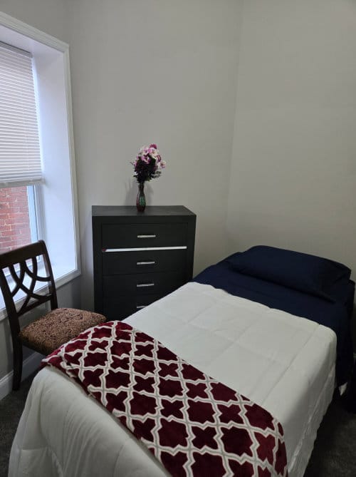 Simple interior of a resident's room with a bed and chair
