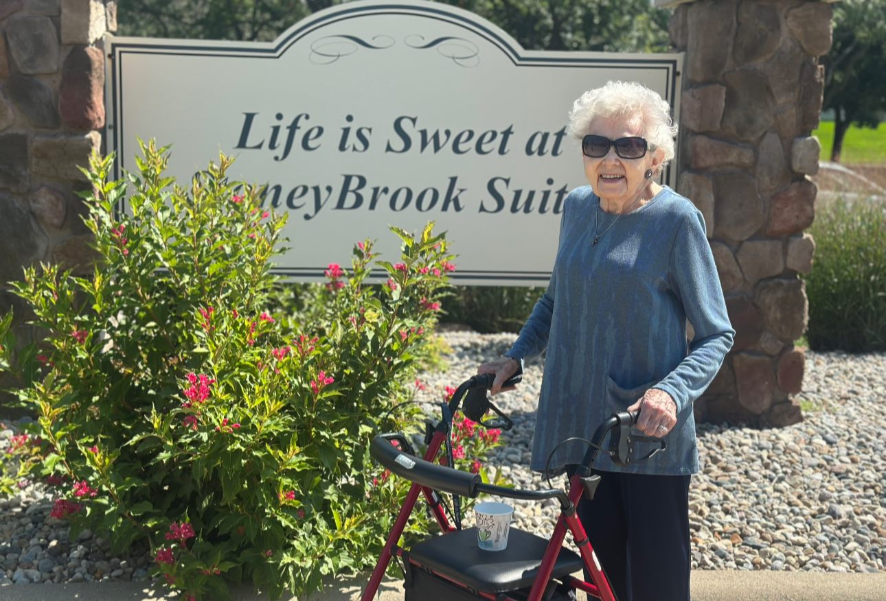 Elderly woman with walker standing near facility sign