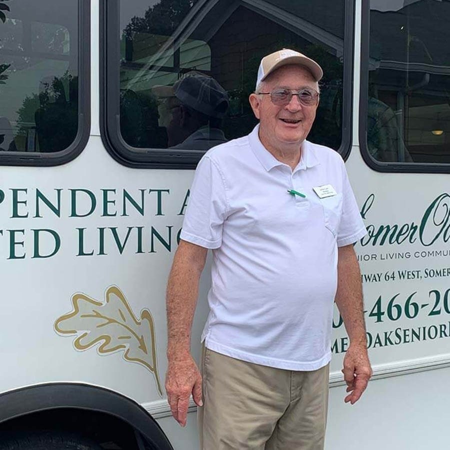 An elderly man smiling by a facility transport bus