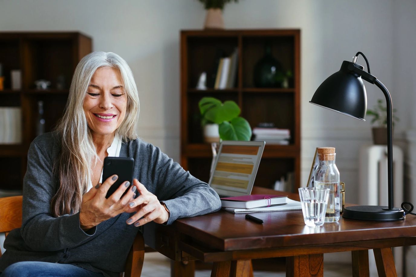 A woman smiling at her phone in a bright room