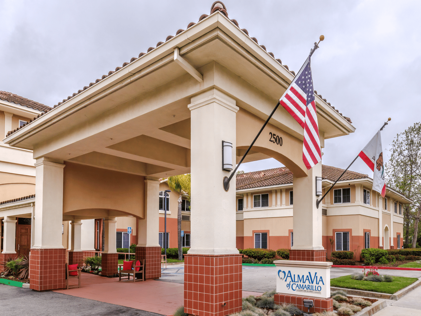 Front entrance of AlmaVia of Camarillo with flags and sign