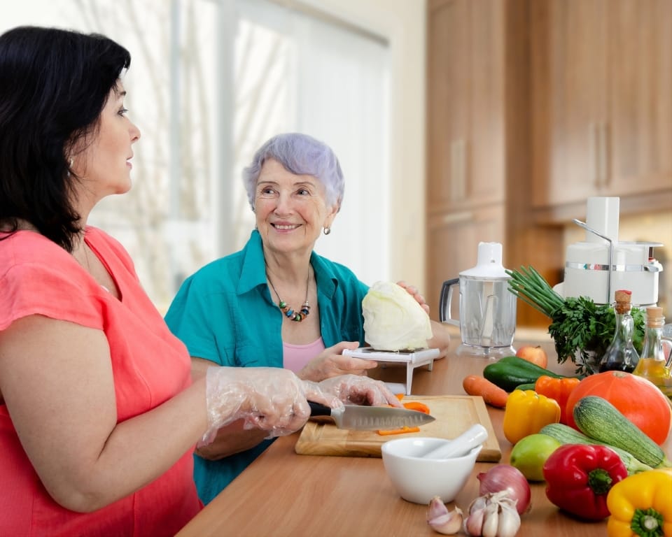 Senior resident and staff member preparing food together in the kitchen