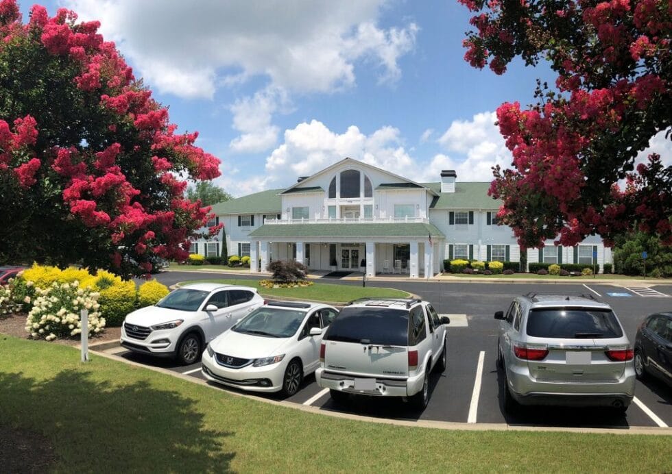 Exterior view of a senior living facility with flowers and vehicles