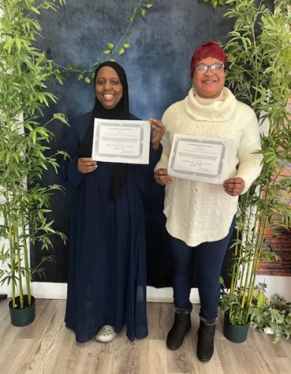Two women holding certificates in a decorated space.