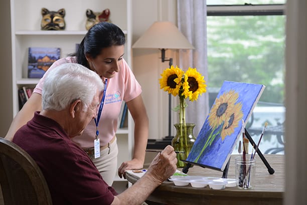 Senior resident painting with caregiver assistance.
