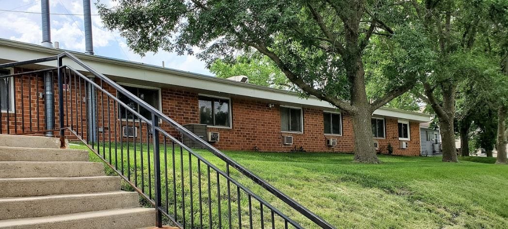 Exterior view of a brick building at Azria Health Park Place with a grassy area and trees