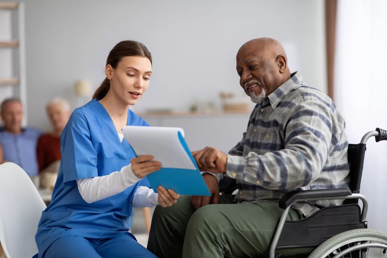 A nurse discusses documents with a male resident in a wheelchair.