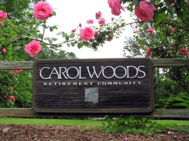 Sign of Carol Woods Retirement Community surrounded by pink roses.
