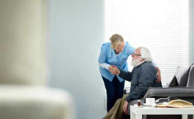 A caregiver and a senior man shaking hands in a cozy living room.