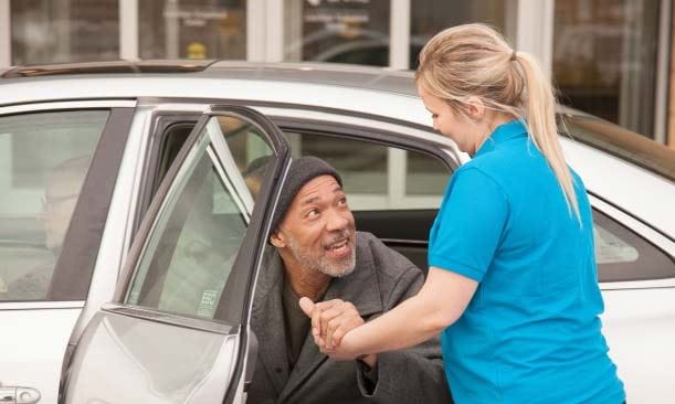 A staff member assisting a resident getting out of a car