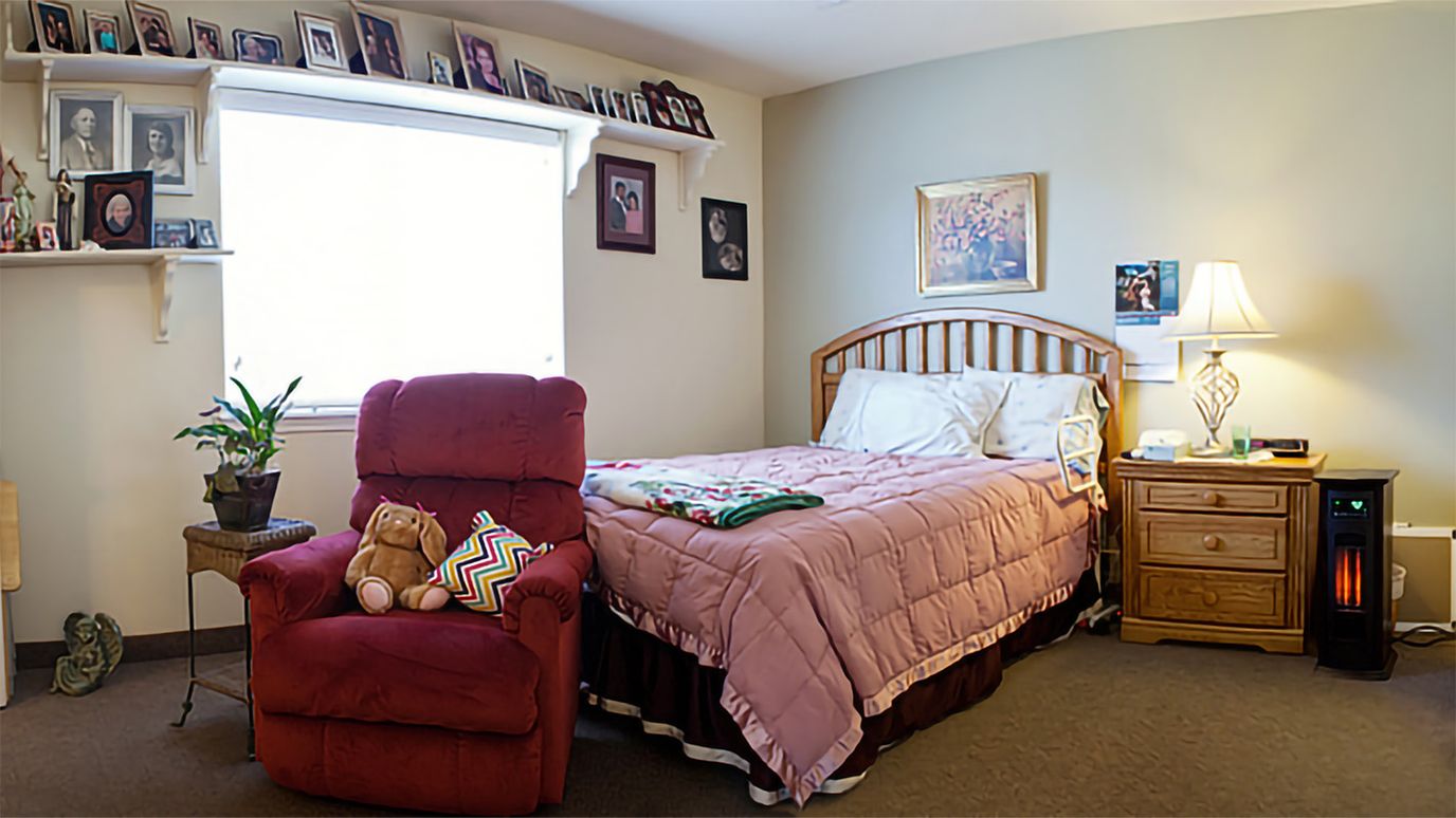 A cozy resident room featuring a bed, red recliner, and personal decor.