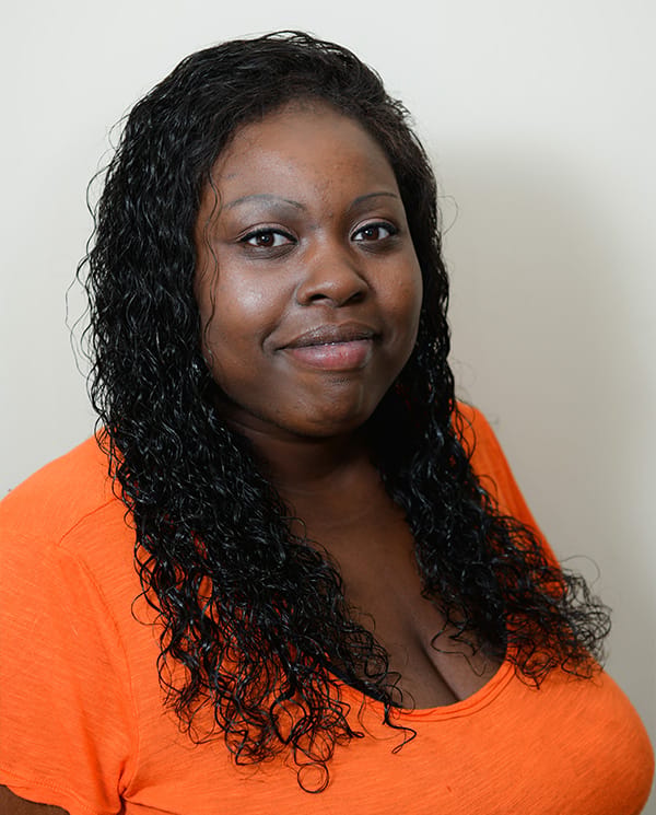 A woman smiling in an orange shirt against a neutral background