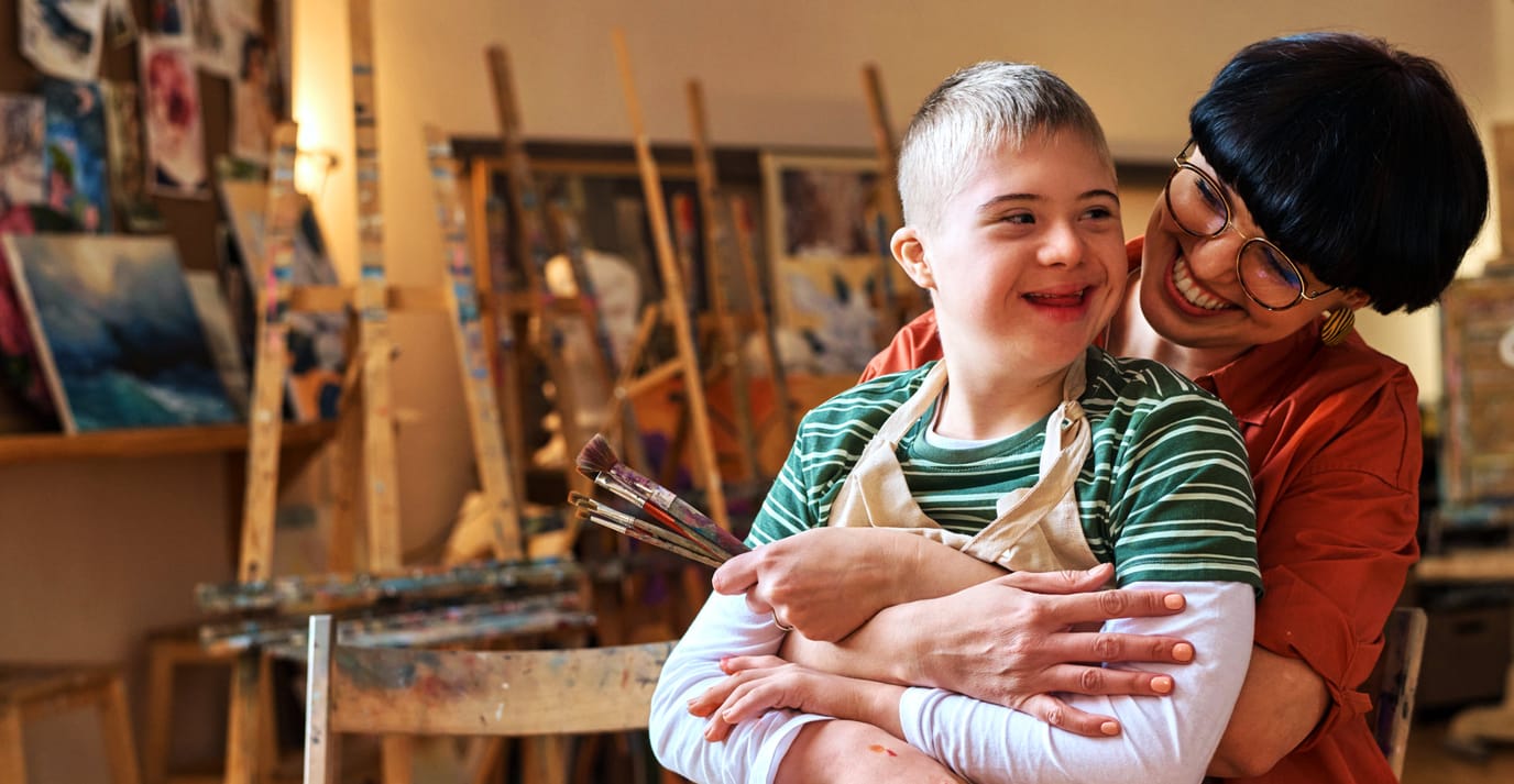 Woman hugging a child with Down syndrome in an art studio.