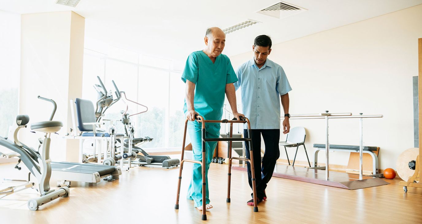 Trainer assisting senior with a walker in a rehabilitation center.