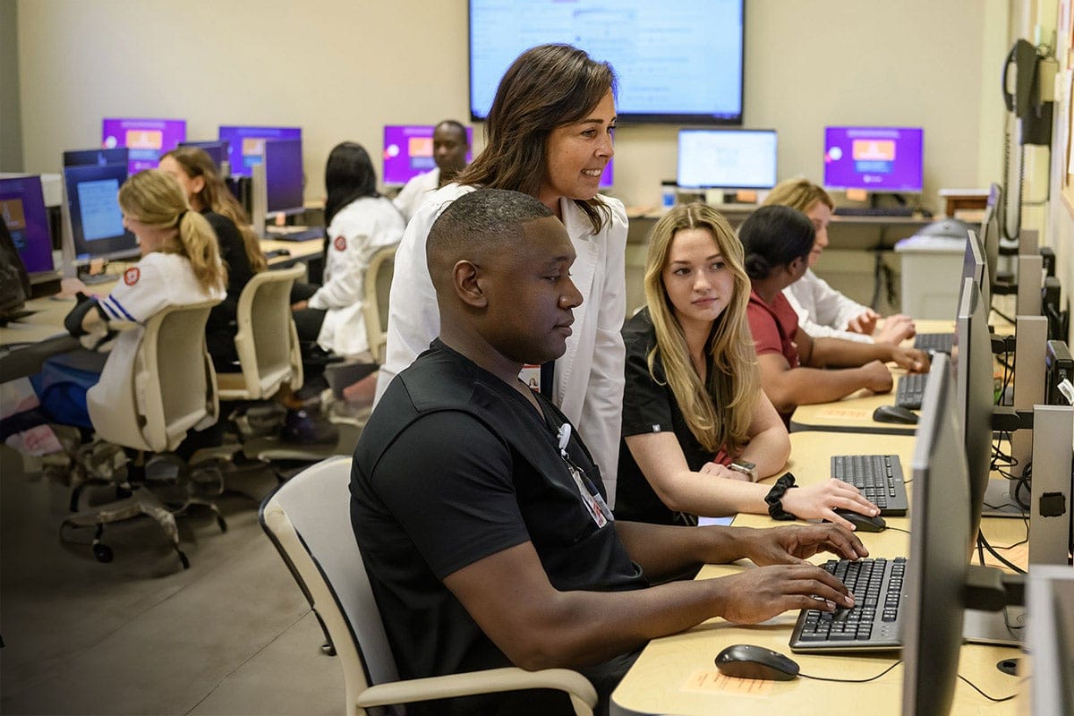 Staff members assisting residents with computers in a tech room