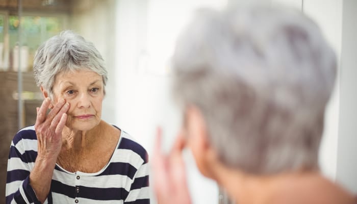 An elderly woman applying cream in front of a mirror
