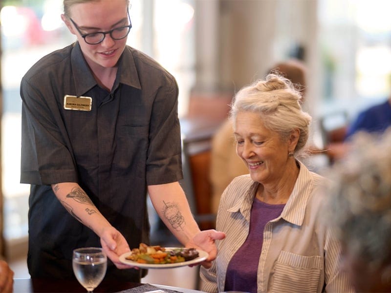 Staff serving food to a smiling resident in the dining area