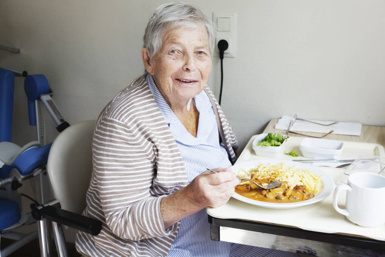 An elderly woman enjoying a meal in her room