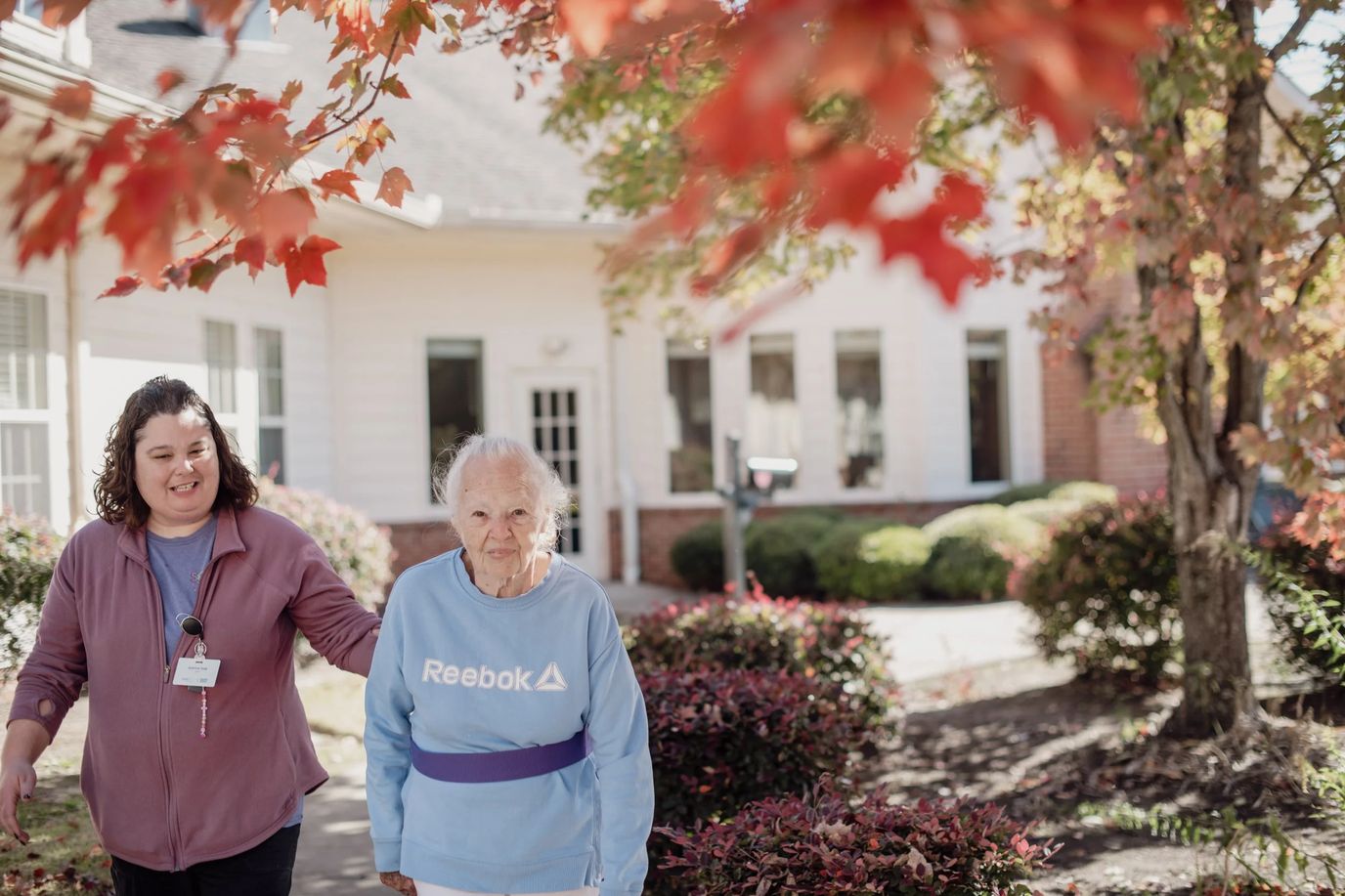 Staff assisting a resident outdoors in a well-kept garden