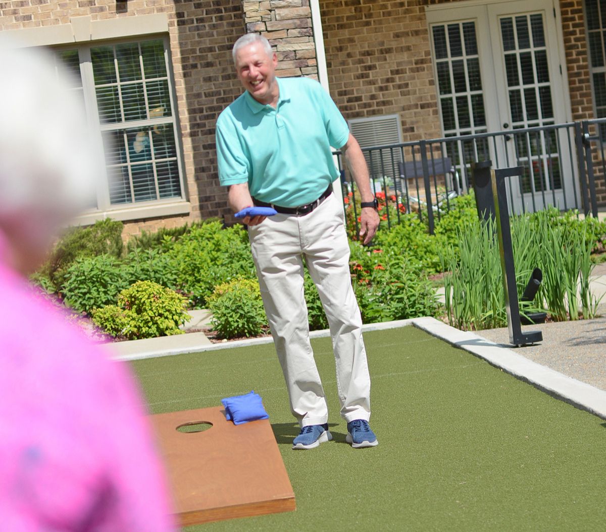 Resident playing corn hole outdoors with building in background