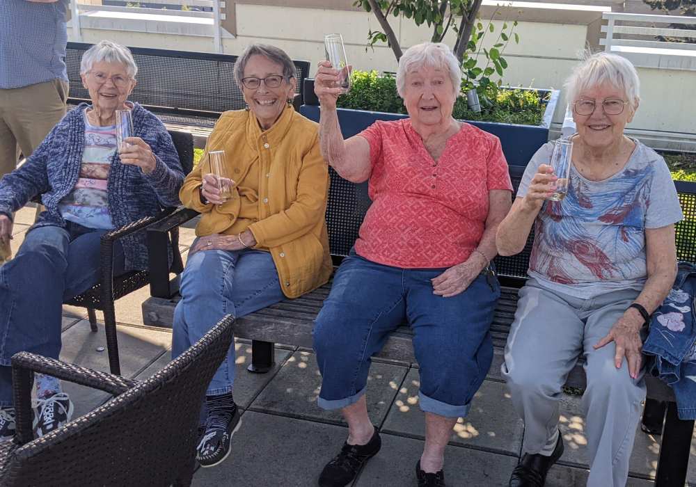 Four elderly women celebrating outdoors with drinks.