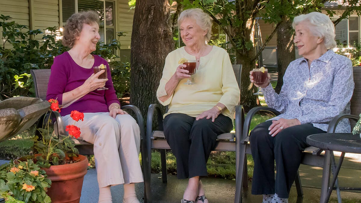 Three residents enjoying drinks outside in a garden area.