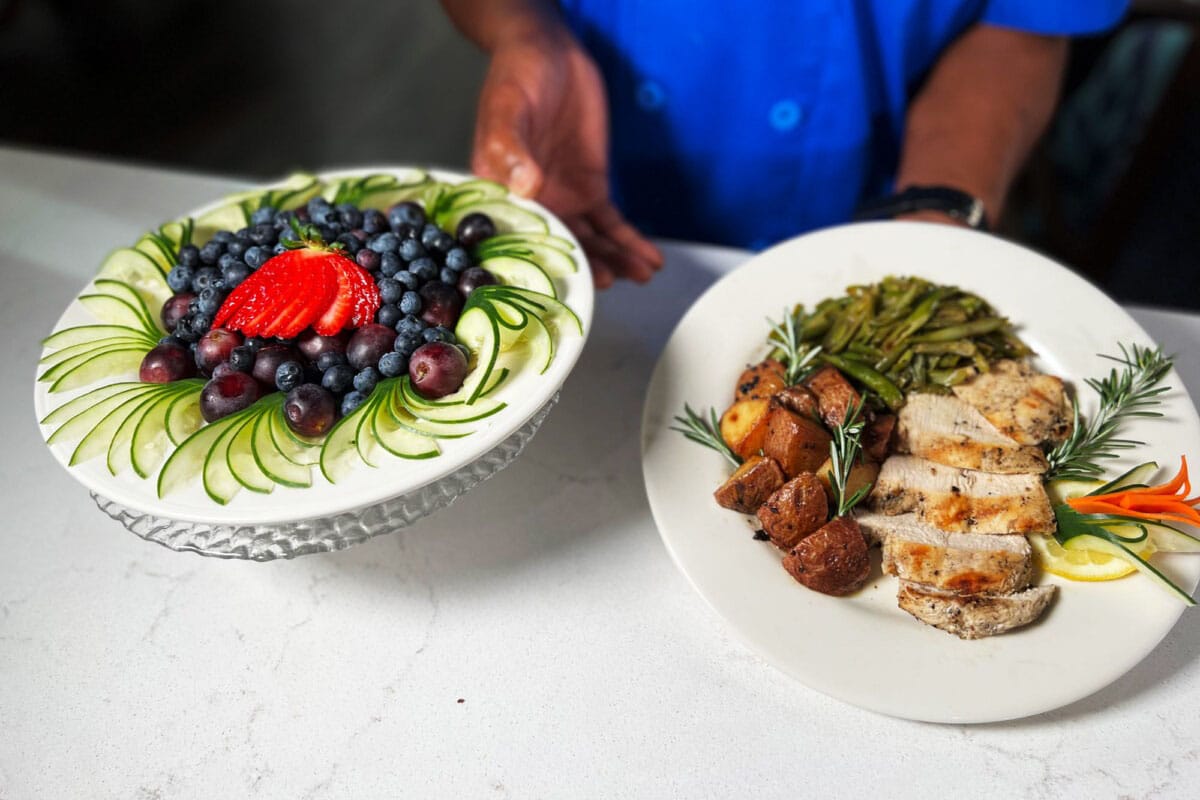 A chef presenting a gourmet meal with vegetables and dessert