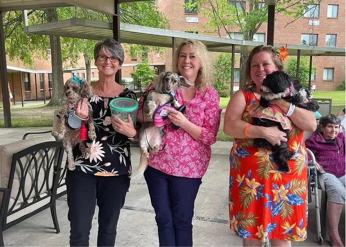 Staff and residents holding small dogs in an outdoor setting