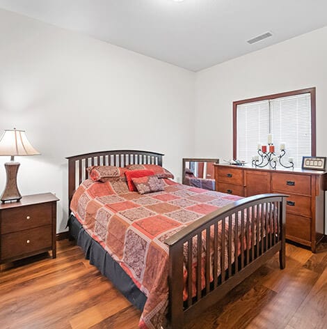 Good Samaritan Society – Grand Island Village, nursing home in Grand Island, NE — Bedroom with a wooden bed and dresser in natural light