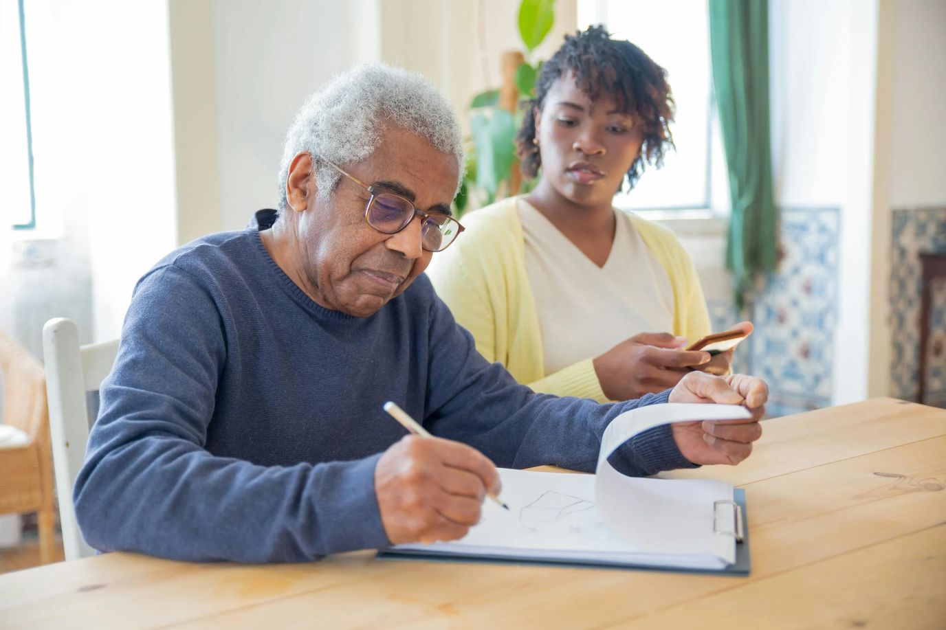 An elderly man drawing with a caregiver's support