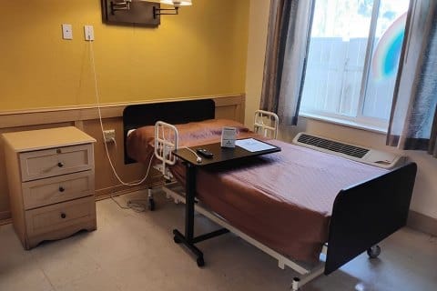 A private resident room with a hospital bed and nightstand
