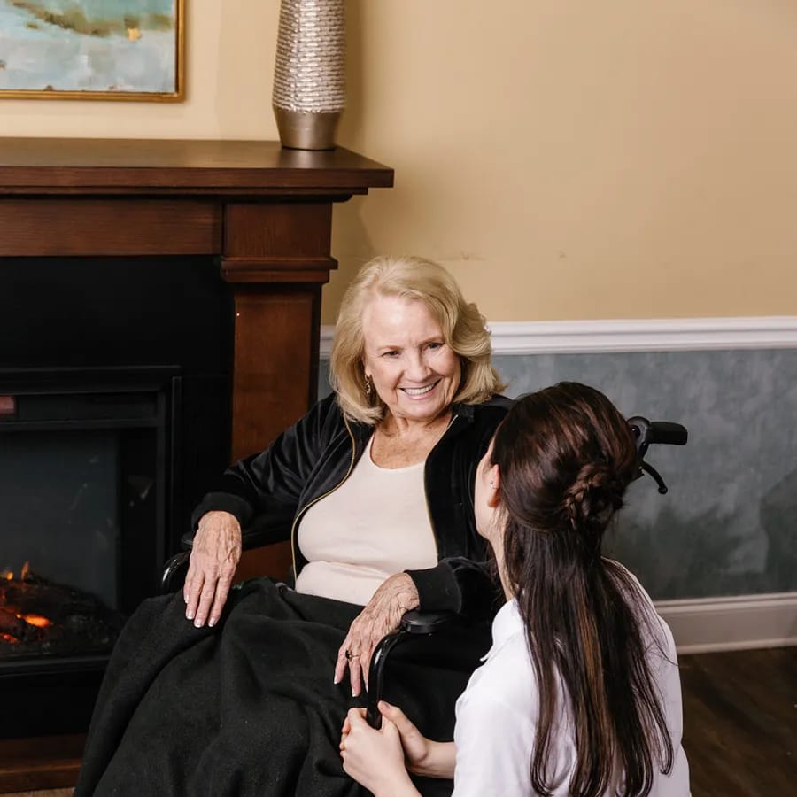 A caregiver talking with a resident by a cozy fireplace