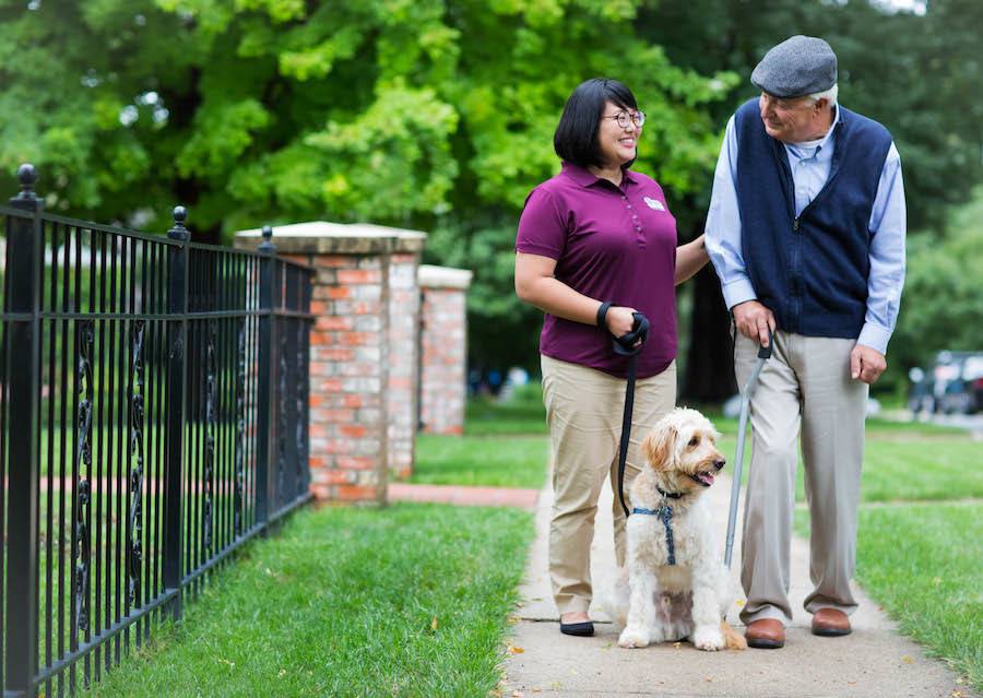 Resident walking with staff and a dog in a garden