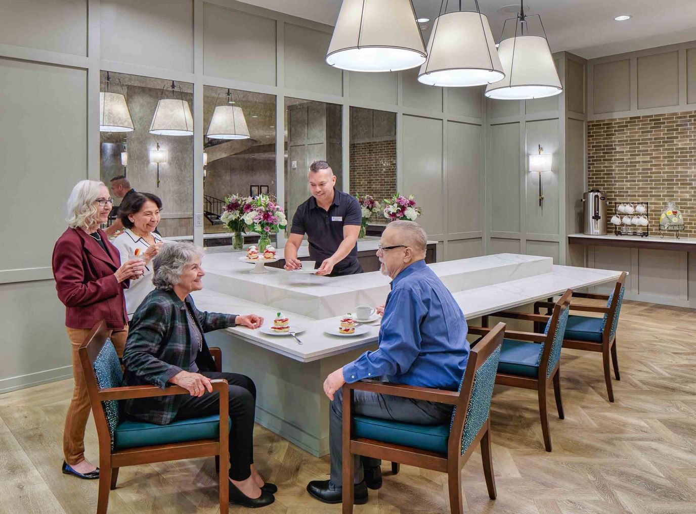 Staff serving food to engaged residents in a dining area.