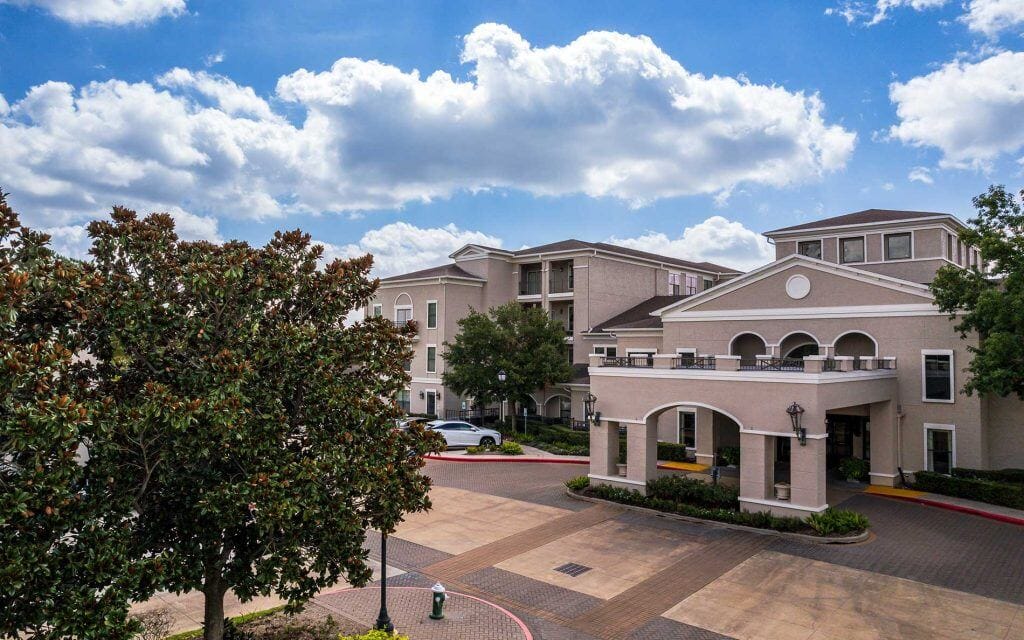 Conservatory at Champion Forest, independent living in Spring, TX — Senior living facility with landscaped entrance and blue sky