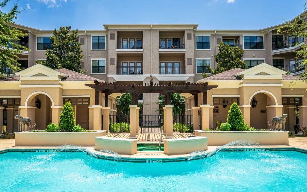 Conservatory at Champion Forest, independent living in Spring, TX — Swimming pool with lush greenery and residential buildings